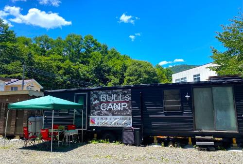 a bus camper with a green umbrella and tables and chairs at BULLsキャンプ 富士の麓 自然に囲まれたペットと泊まれるゲストハウス Guesthouse with pets at the foot of World Heritage Mt Fuji in Fujikawaguchiko