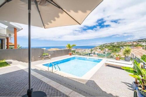 a villa with a swimming pool and an umbrella at Luxury Haven: Heated Pool, AC & Sun in Ponta do Sol