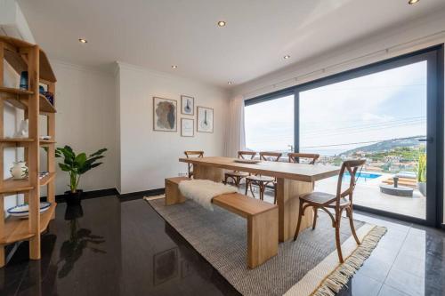 a dining room with a table and chairs and a large window at Luxury Haven: Heated Pool, AC & Sun in Ponta do Sol