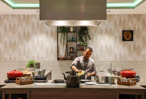 a man standing in a kitchen preparing food at Leonardo Royal Hotel Amsterdam in Amsterdam