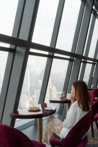 a woman sitting at a table with a cup of coffee at Ascott Embassy Sathorn Bangkok in Bangkok