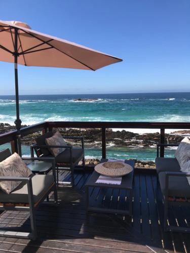 a deck with chairs and an umbrella and the ocean at On the Rocks @ Eersterivier in Eersterivierstrand