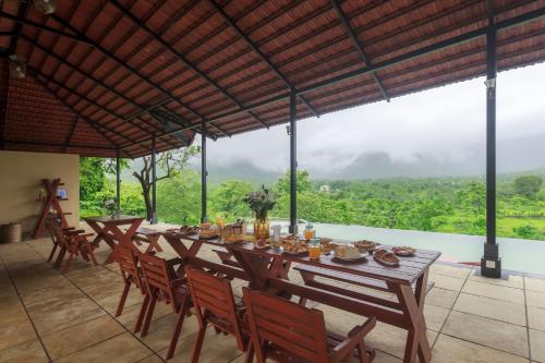 a dining room with a table and chairs and a view at StayVista's Basalt - with Mountain Views, Infinity Pool, Vintage Interiors, and Games Room in Karjat
