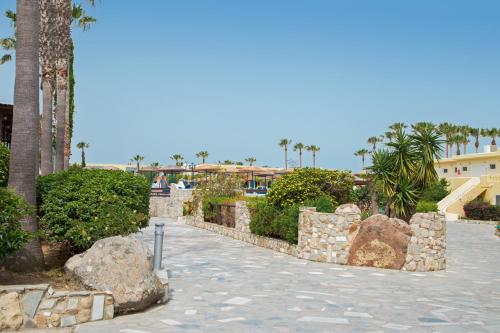 a walkway with rocks and palm trees and a building at Eurovillage Achilleas Hotel in Mastichari