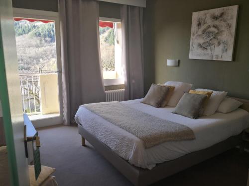 a bedroom with a white bed with two windows at Logis Hôtel-Restaurant Le Tanargue in Valgorge