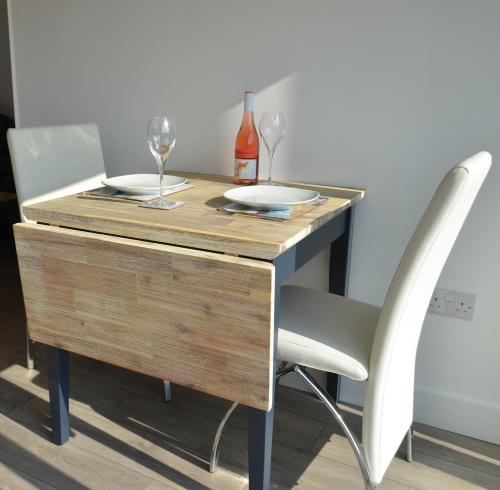 a wooden table with two glasses and two plates on it at Swn Y Mor - Sound of the Sea - by Aberporth Beach Holidays in Aberporth