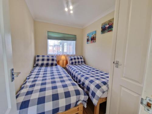 two beds in a room with blue and white checks at 169 Broadside Holiday Chalet near Broads & Beaches in Stalham