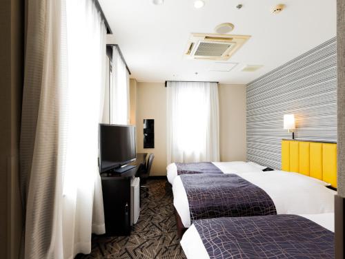 a hotel room with two beds and a flat screen tv at APA Hotel Fukuoka Yukuhashi Ekimae in Yukuhashi