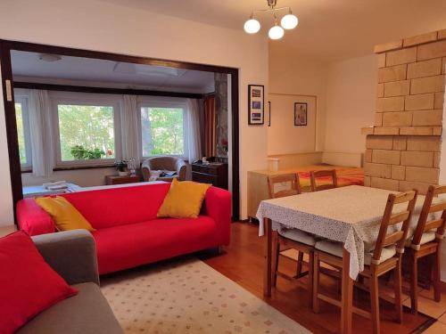 a living room with a red couch and a table at Csendes pihenés az erdő mellett - Madárfüttyös Vendégház in Pilisszentlászló