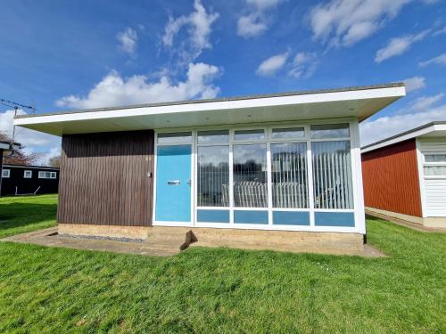 a small building with a blue door on the grass at 67 Broadside Holiday Chalet near Broads & Beaches in Stalham