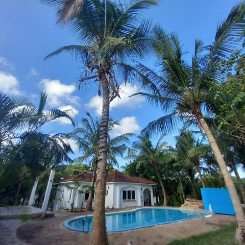 dom z dwoma palmami obok basenu w obiekcie Maasai Barracks Resort w mieście Mombasa