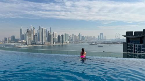 uma mulher sentada numa piscina de beiral infinito com vista para uma cidade em First Class Apartments in Seven Palm with direct Access to the West Palm Beach and Nakheel Mall em Dubai