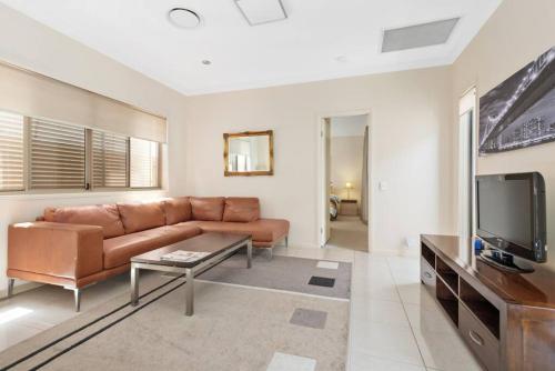 a living room with a brown couch and a tv at Impeccable Modern 1 Bedroom Apartment ~ Taringa in Brisbane