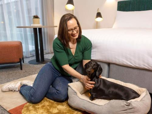 坎培拉的住宿－The Sebel Canberra Campbell，坐在地板上的女人,在床上抱着狗