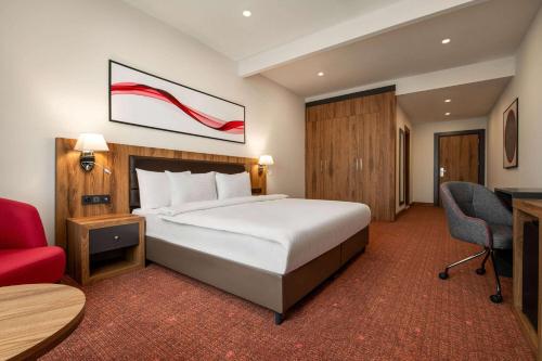 ブルサにあるRamada by Wyndham Karacabeyのベッドと赤い椅子が備わるホテルルームです。