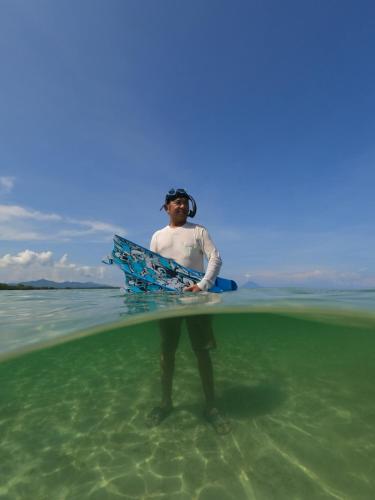 mężczyzna stojący w wodzie z deską surfingową w obiekcie Camping Rein apwisindo desa sarawet w mieście Likupang