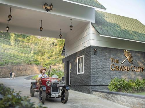 a woman driving an old red car in front of a building at The Grand Cliff Resort Munnar in Viripara