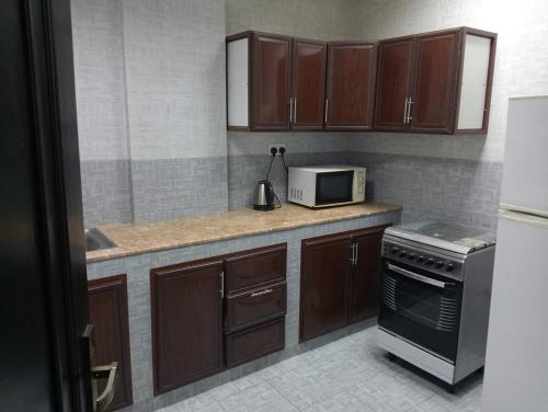 eine Küche mit braunen Schränken und einer weißen Mikrowelle in der Unterkunft JANDOUL SALALAH جندول صلاله in Salalah
