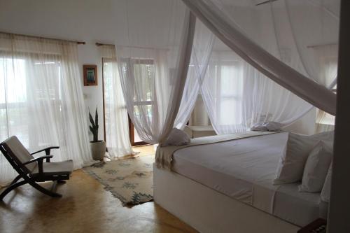 a bedroom with a canopy bed and a chair at Dar Beach House - Michamvi in Michamvi