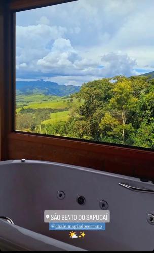a bath tub in front of a window with a view at Chalé Magia do Serrano in São Bento do Sapucaí