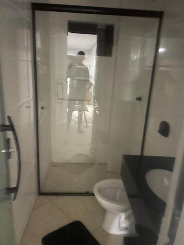 a bathroom with a toilet and a person sitting in a chair at Sol-v-mar in Penha