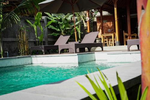 a swimming pool with chairs and an umbrella at The Banana’s Kumbe Villa in Tampaksiring