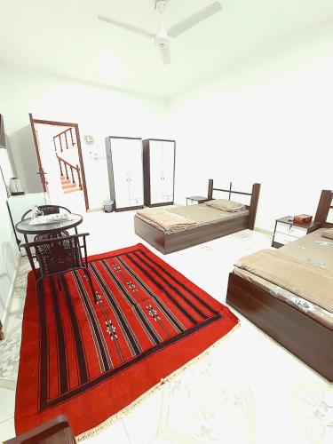 Habitación con 3 camas y alfombra roja. en البيت الابيض, en Mawāliḩ