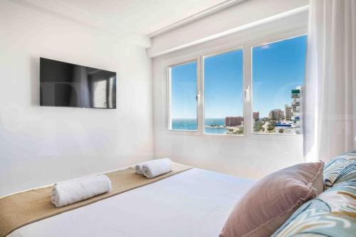 Un dormitorio con una cama y un televisor y ventanas. en Seaview coastal apartment in Benalmadena by REMS, en Benalmádena
