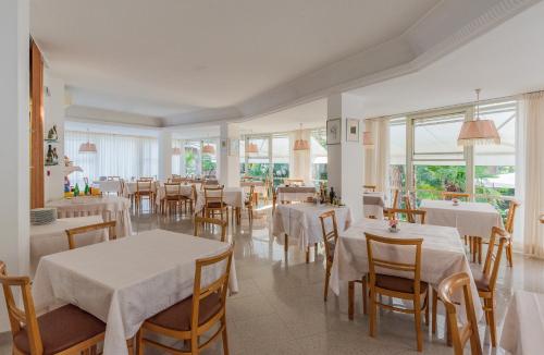 un restaurante con mesas y sillas blancas y ventanas en Hotel Escorial, en Cervia