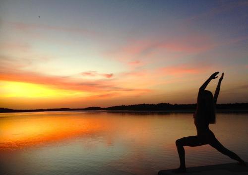 a woman doing a yoga pose in front of a body of water at Les Palétuviers in Toubakouta