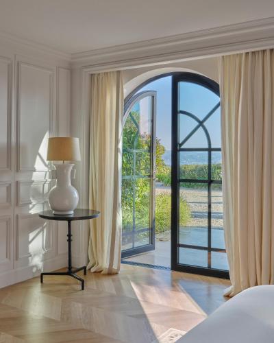 a bedroom with a large window and a table with a lamp at Airelles Château de la Messardière in Saint-Tropez