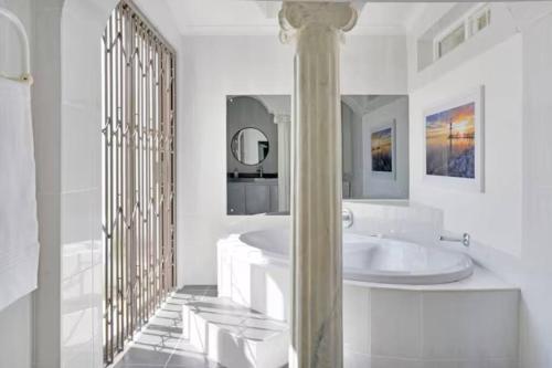 a white bathroom with a tub and a mirror at The Bakoven Rock in Cape Town