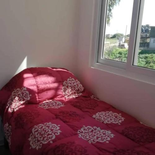 a red bed in a room with a window at Hermoso Departamento El Tabo in El Tabo