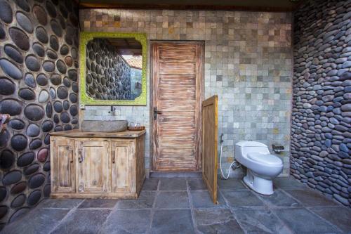a bathroom with a toilet and a sink and a wooden door at Global Royal Pemuteran in Pemuteran