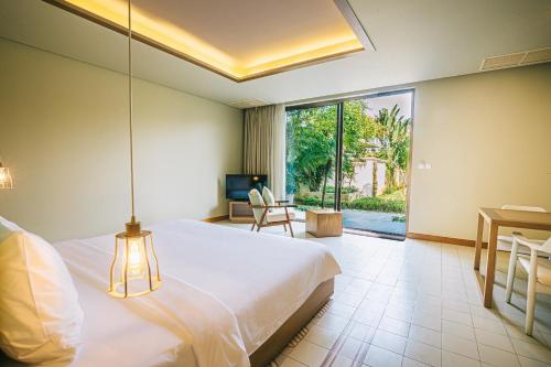 a bedroom with a bed and a desk and a window at The Victoria Resort Sam Son in Sầm Sơn