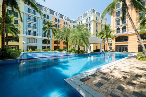 a large swimming pool with palm trees and buildings at Pacific Apartment & Hotel Phu Quoc in Phu Quoc