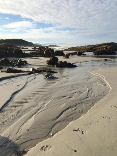 a beach with some rocks and sand and water at Hermanus Backpackers & Budget Accommodation in Hermanus