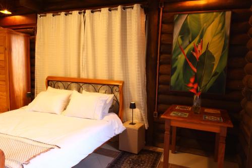 a bedroom with a bed and a table and a painting at Aldeia Flor de Liz - Pedra Azul in Pedra Azul