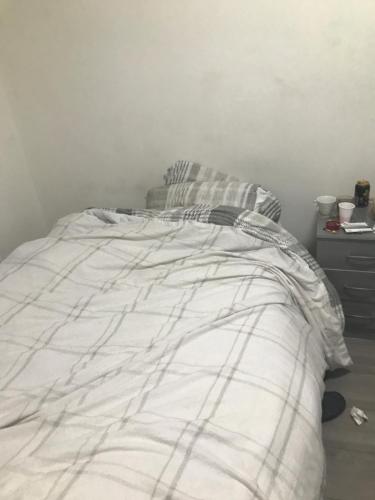 a bed with a white blanket and a night stand at Luxx apartment in Erith