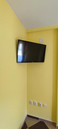 einen Flachbild-TV, der an einer gelben Wand hängt in der Unterkunft Apartmani Ad fines in Kuršumlija