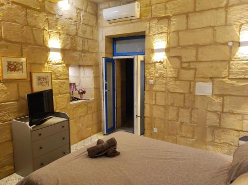 a bedroom with a bed and a tv and a stone wall at Il Hnejja Farmhouse in Mqabba