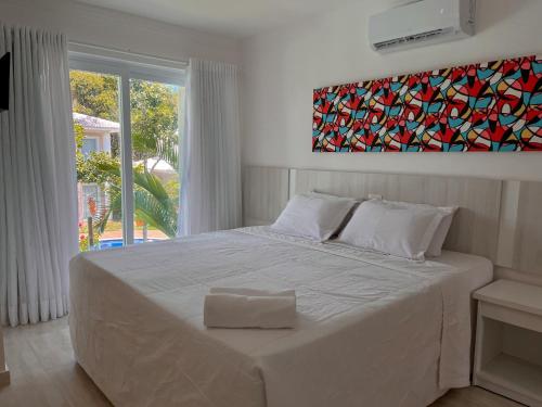 a white bed in a bedroom with a painting on the wall at 7 Heaven Arraial D'ajuda - Alto da Pitinga - Ararat in Arraial d'Ajuda