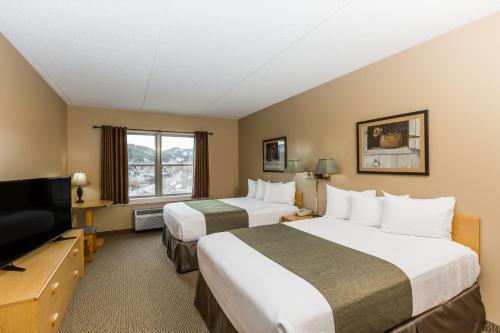 a hotel room with two beds and a flat screen tv at Travelodge by Wyndham Deadwood in Deadwood
