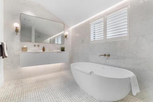 a white bathroom with a tub and a mirror at Arrowtown Mountain Views in Arrowtown