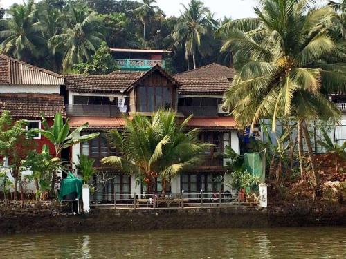 una casa a orillas de un río con palmeras en WOODEN CHALET ON THE RIVER BANKS en Old Goa