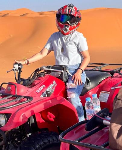 a person standing next to a red atv in the desert at Luxury Bedouin Camp in Merzouga
