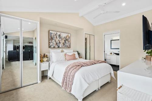 a white bedroom with a bed and a bathroom at HEATed Pool, Lake & Beach, Luxury 5 B/R House in Lake Illawarra
