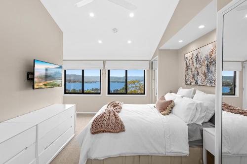 Schlafzimmer mit einem weißen Bett und Fenstern in der Unterkunft HEATed Pool, Lake & Beach, Luxury 5 B/R House in Lake Illawarra