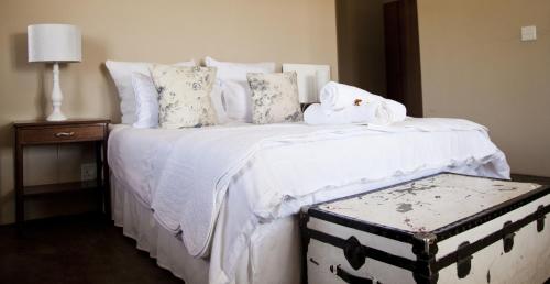 a bedroom with a white bed with a trunk on it at Guinevere Guest Farm in Tulbagh