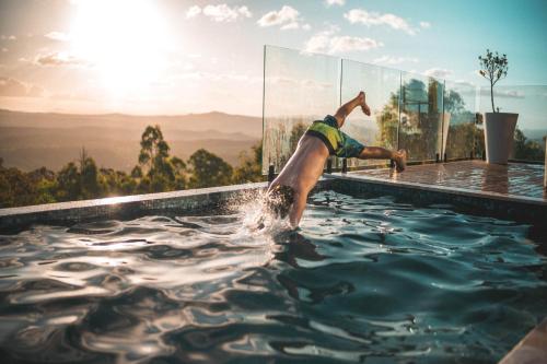 a man in a swimming pool with the sun behind him at Luxurious Hinterland Guest House with HEATED POOL Sleeps 10 Brisbane Scenic Rim Gold Coast in Canungra
